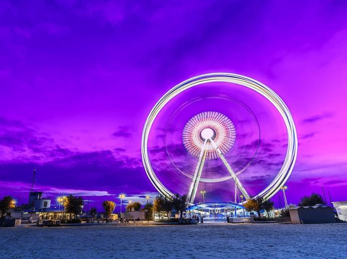 Lit Ferris wheel with purple sunset sky.